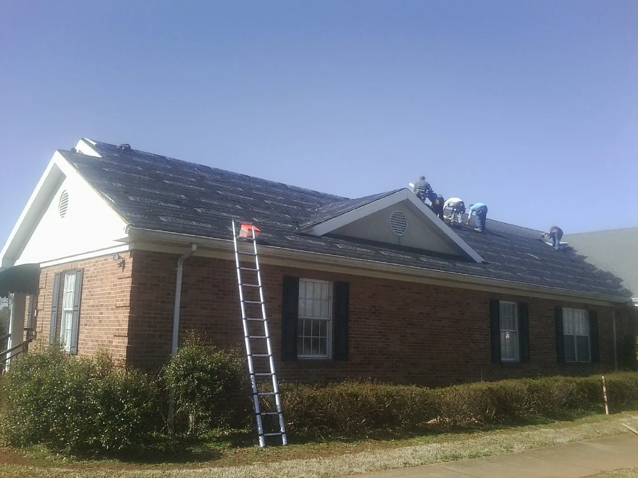 Crew tearing shingles off a brick ranch roof with a ladder set — Emergency Roof Repair work by our crew in Lecompton