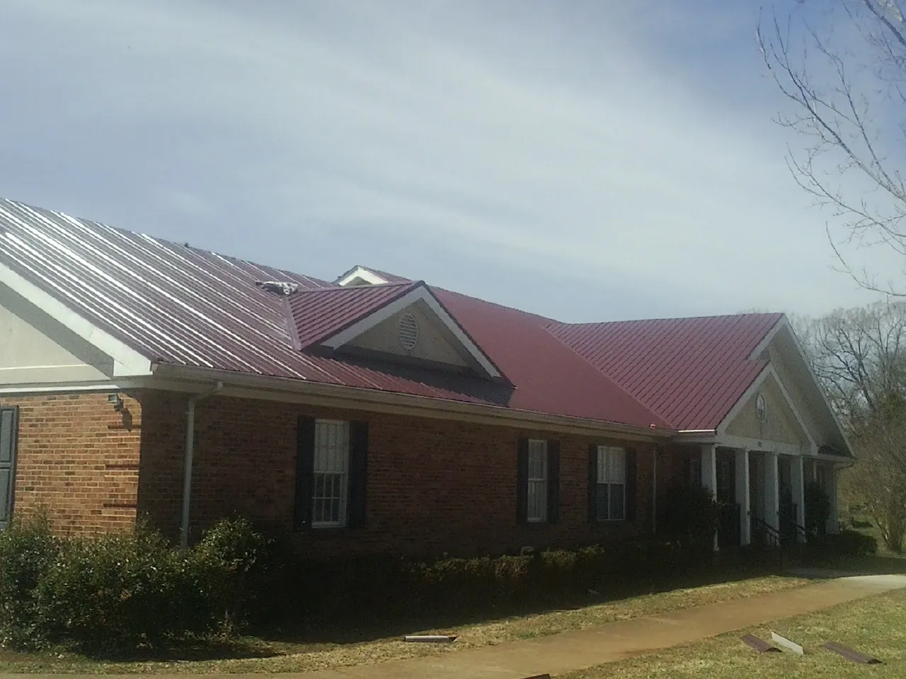 Red metal roof with gabled entries on a long brick building, from a Hail Damage Roof Repair job in Lecompton