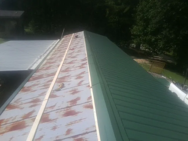 Old rusted panels beside newly installed green metal roofing — Wind Damage Roof Repair by Roofing Brothers in Lecompton