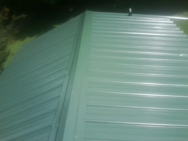 New green metal panels meeting at the ridge of a roof — Flat Roof Repair work by our crew in Lecompton