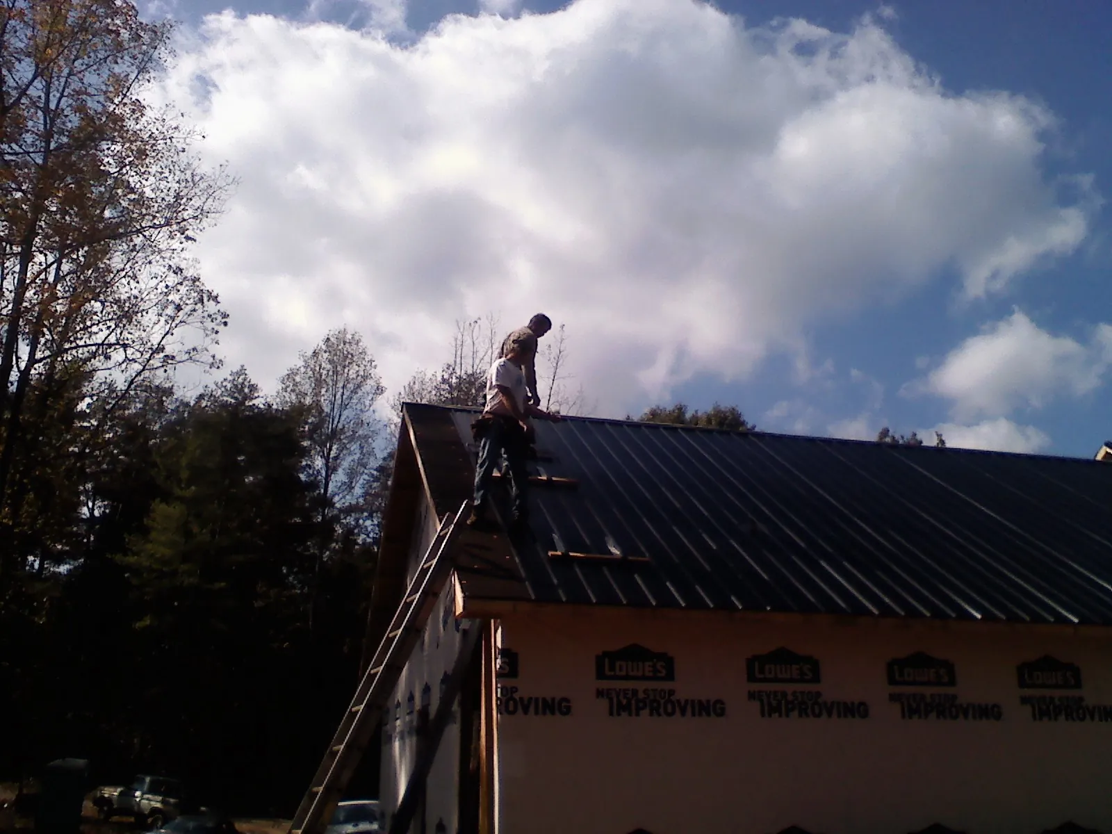 Roofer fastening dark metal panels high against a cloudy sky, from a Roof Inspection job in Lecompton